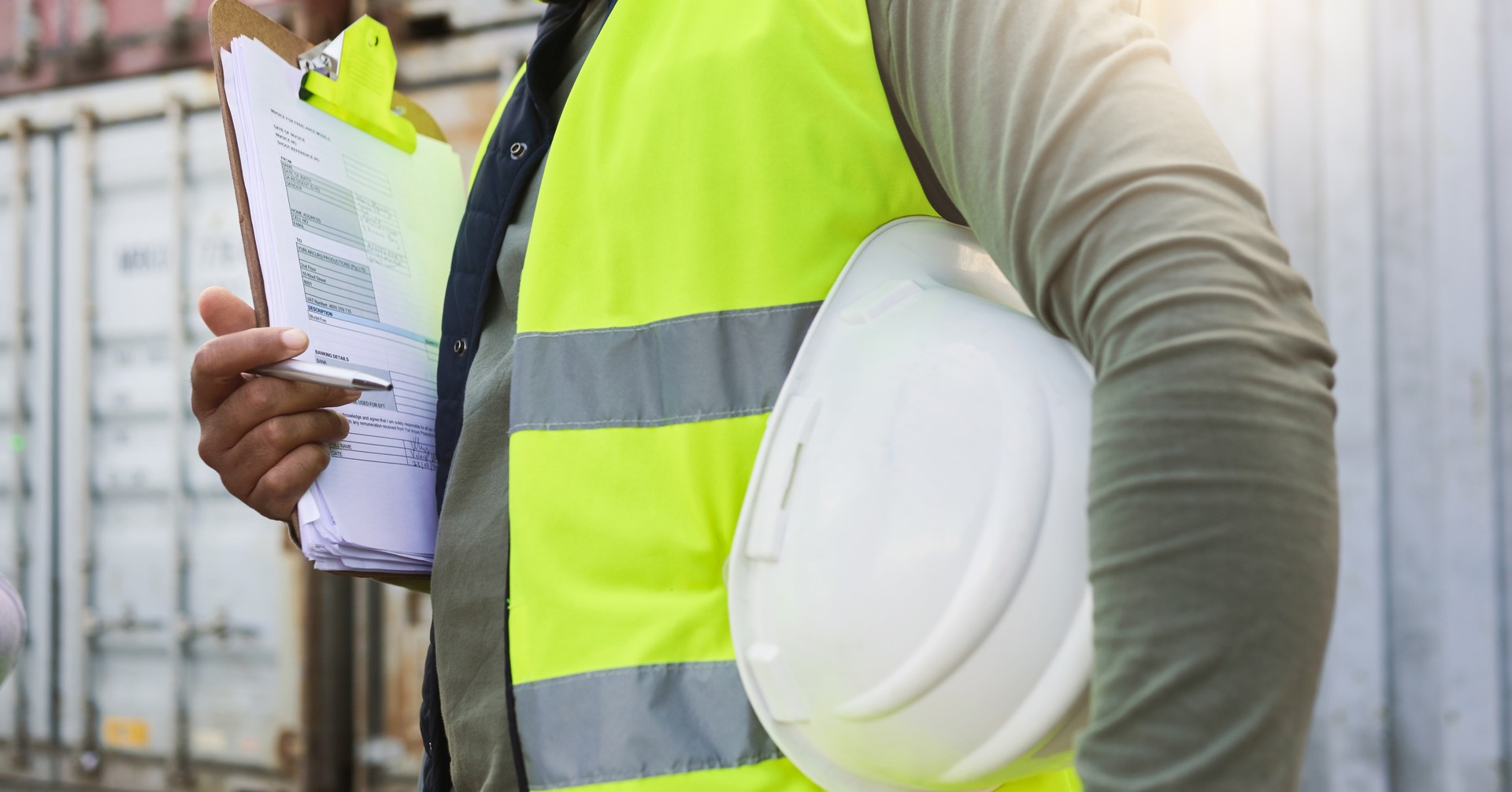 Man, checklist and work in logistics with helmet by container at port. Black man, notes and pen in hand to check stock while working in shipping, cargo and transportation industry in Cape Town